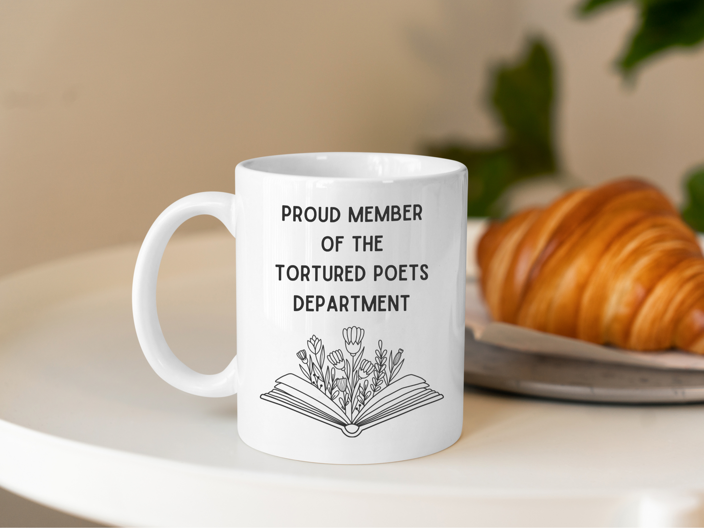 A white ceramic mug with a drawing of a book with flowers, above it is the text Proud member of the Tourtured Poets Department on the front. This is a 10oz mug which is perfect for fans of Taylor Swift. Made and sold by Krissi's Creations.