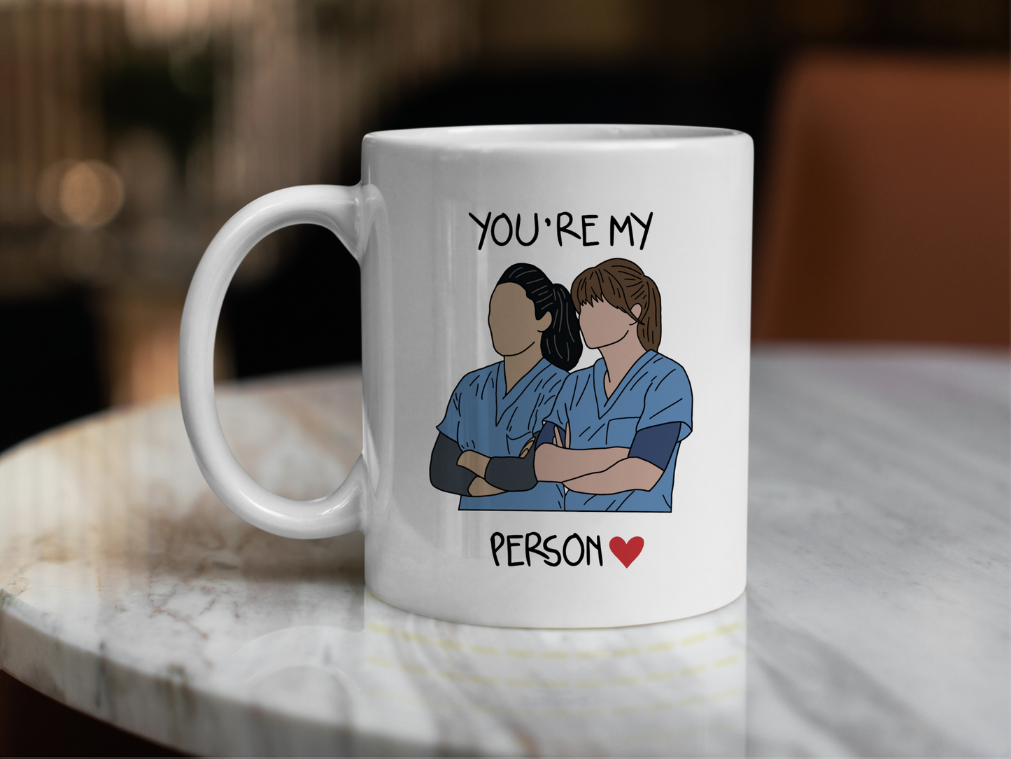 A white ceramic mug with a drawing of Meredith Grey and Cristina Yang from Grey's Anatomy on the front with the text You're my person. This is a 10oz mug which is perfect for fans of Grey's Anatomy, particularly the characters Meredith Grey and Cristina Yang. Made and sold by Krissi's Creations.