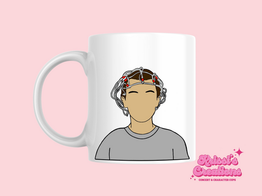 A white ceramic mug with a drawing of Eleven from Stranger Things on the front. This is a 10oz mug which is perfect for fans of Stranger Things, particularly the character Eleven. Made and sold by Krissi's Creations.