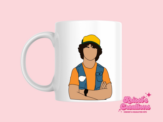 A white ceramic mug with a drawing of Dustin Henderson from Stranger Things on the front. This is a 10oz mug which is perfect for fans of Stranger Things, particularly the character Dustin Henderson. Made and sold by Krissi's Creations.