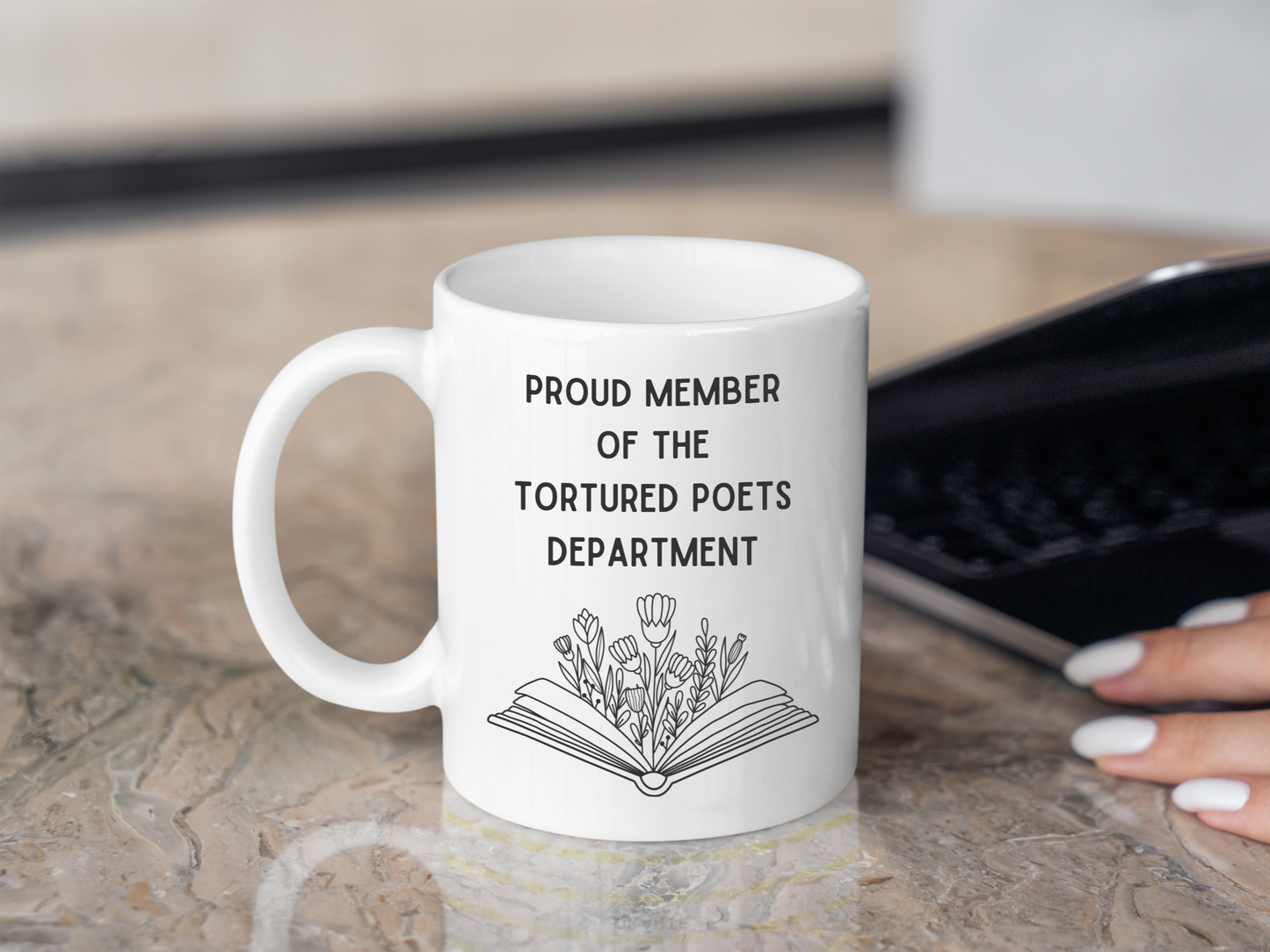 A white ceramic mug with a drawing of a book with flowers, above it is the text Proud member of the Tourtured Poets Department on the front. This is a 10oz mug which is perfect for fans of Taylor Swift. Made and sold by Krissi's Creations.