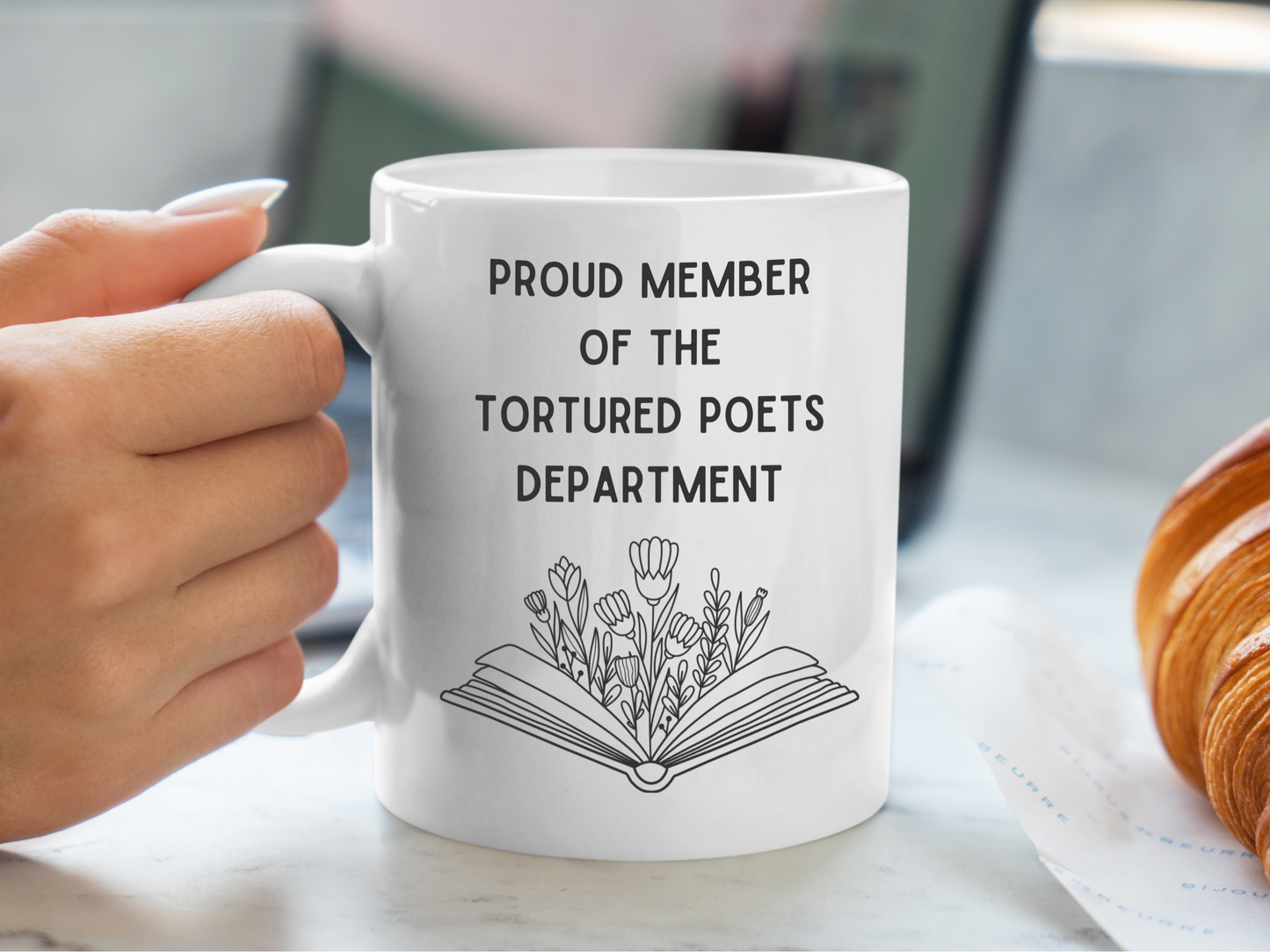 A white ceramic mug with a drawing of a book with flowers, above it is the text Proud member of the Tourtured Poets Department on the front. This is a 10oz mug which is perfect for fans of Taylor Swift. Made and sold by Krissi's Creations.