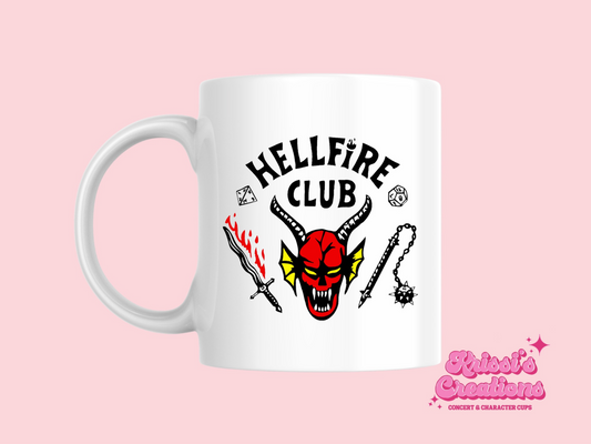 A white ceramic mug with a drawing of the Hellfire Club logo from Stranger Things on the front. This is a 10oz mug which is perfect for fans of Stranger Things, particularly the character Eddie Munson who wears the Hellfire Club logo. Made and sold by Krissi's Creations.