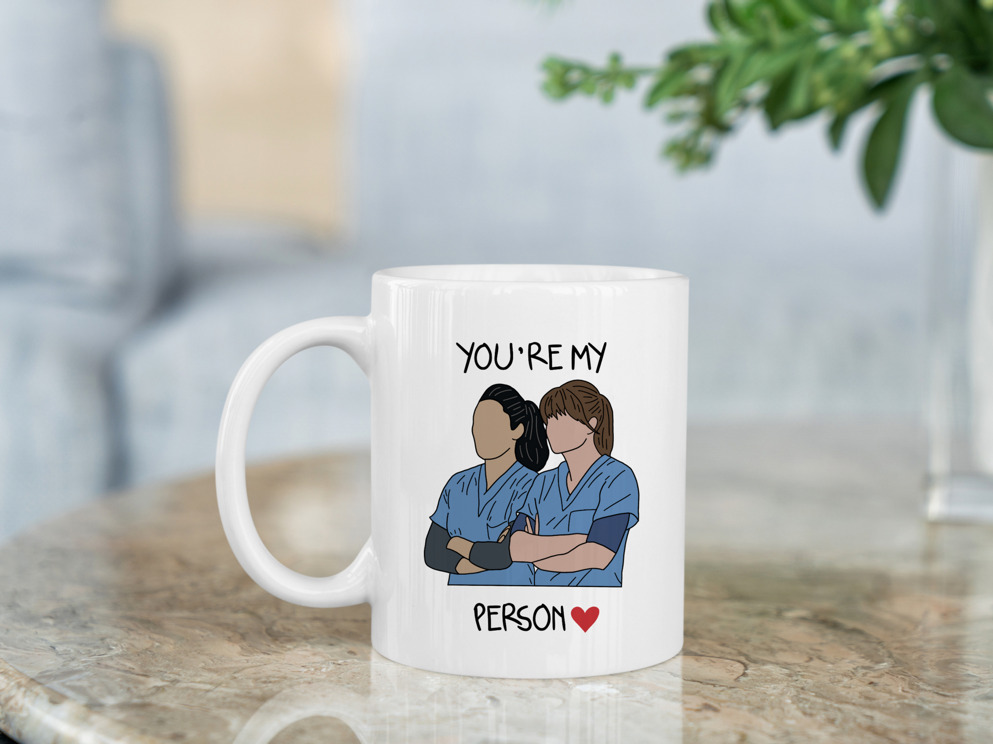 A white ceramic mug with a drawing of Meredith Grey and Cristina Yang from Grey's Anatomy on the front with the text You're my person. This is a 10oz mug which is perfect for fans of Grey's Anatomy, particularly the characters Meredith Grey and Cristina Yang. Made and sold by Krissi's Creations.